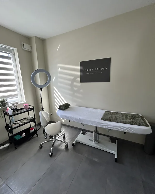Behandlungsraum im Curbet Studio mit Liege, Arbeitshocker und Schild an der Wand